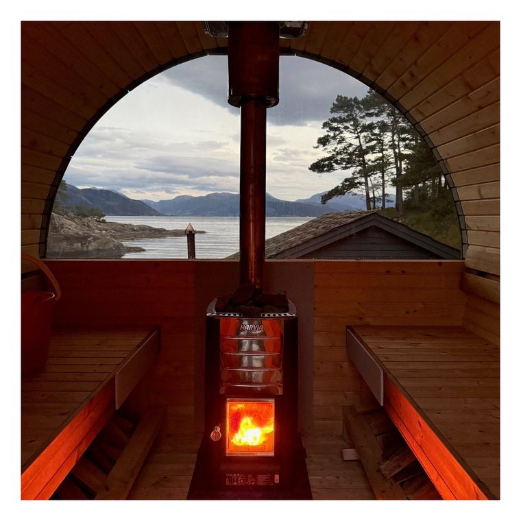 Innvendig i tønnebadstua med fyr i vedovnen og fjorden gjennom vinduet